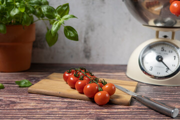 A panicle cocktail tomato lies on a cutting board. In the background is basil and a scale