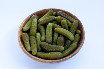 Pickled gherkins or cucumbers in wooden bowl on white background.