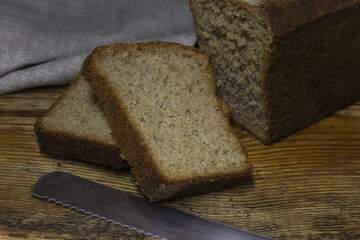 Loaf of brown, organic rye bread on black background. Two slices of sliced bread. Place for text. Banner for a design project.