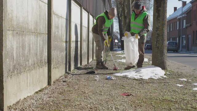 two retired volunteers picking up trash along the street using trash picker stick