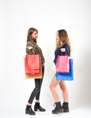 Two female friends holding shopping bags while standing on an isolated background.