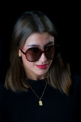Stylish brunette woman wearing sunglasses on a dark isolated background.