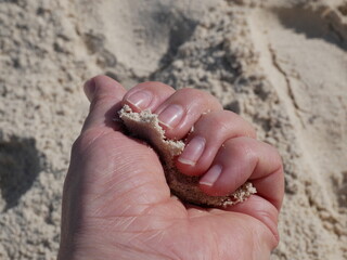 A woman's hand holds a handful of sand against the background of the shore on a sunny summer day on a summer vacation. Nails without manicure