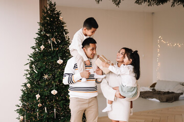 A happy diverse Asian family celebrates Christmas. Parents with children give gift boxes decorate the Christmas tree and prepare for the New Year holiday in a decorated house. Selective focus