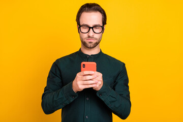 Photo of serious confident young man wear smart casual outfit glasses chatting modern device isolated yellow color background