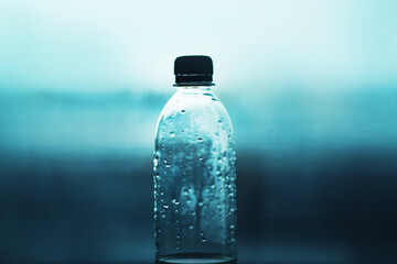 One plastic transparent bottle with a black stopper half filled with clean water is on a blue...