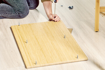 Flat furniture package is assembled at home, buyer installs dowels into slots using screwdriver.