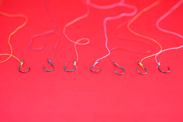 Many empty fishing hooks tied with colored ropes lay on a red ba