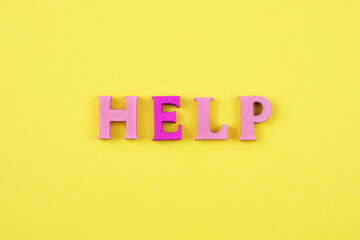 The word help from wooden bright letters on a yellow background. The concept of asking for help, looking for opportunities for help, social support. Creative concept.