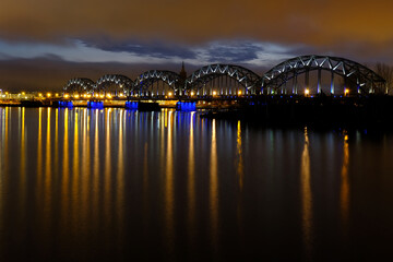Obraz premium Reflection of night lights at dawn on the Daugava in Riga against the background of the railway bridge