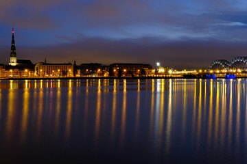Fototapeta na wymiar Reflection of night lights at dawn on the Daugava in Riga against the background of the railway bridge