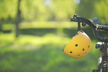 Safety helmet for children, yellow, hanging on the bicycle handlebar.