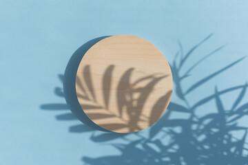Abstract minimal scene of a geometrical form. A cylindrical wooden podium on a pastel blue background with a shadow of tropical palm leaves. Scene to show cosmetic podructs. Showcase, display case