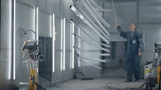 A working molar pulls out parts from the baking oven. Plant for the production of steel metal products. Painting workshop