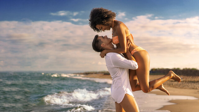Multiracial couple on the beach - Young lovers having fun at sunset - a boyfriend picks up his woman on the beach - Powered by Adobe