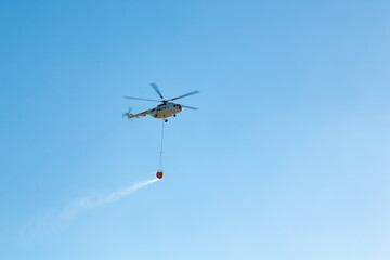 Helicopter going to fire area to extinguish forest fire.  Helicopter with a water bucket on a blue sky. One of the most effective ways to reach fire areas.
