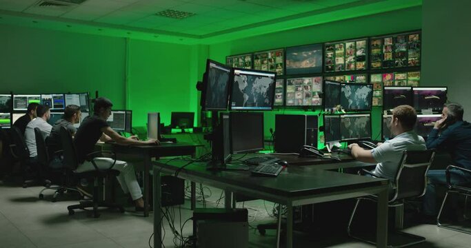 Male workers sitting near computers on monitoring room and working . Programmers or engineers using many laptops , computers , searching , following information and statistics . Cyber security office 
