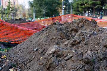 Pile of dirt at the construction site with safety orange net in the background