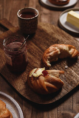 Fototapeta premium Freshly baked cardamom knot buns (also sweet rolls or swirl buns) with cocoa mug and butter and jam on wooden table. Cosy winter breakfast. Selective focus
