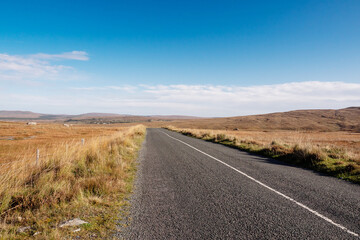 Small narrow asphalt road in a huge empty fields. Clean blue cloudy sky. Warm sunny day. Connemara, Ireland. Travel and transportation concept