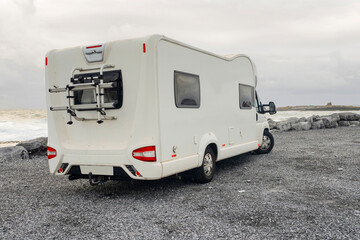 Rear side of a white camper van parked by the ocean. Travel in comfort. Motor home with rack for bicycles in a parking lot. Cloudy sky. Comfortable holiday on a road concept.