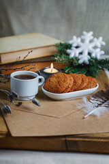 Obraz na płótnie Canvas Oatmeal cookies with hot tea on a natural wood kitchen board. Winter composition for the interior with snow-covered branches, feather and envelope.