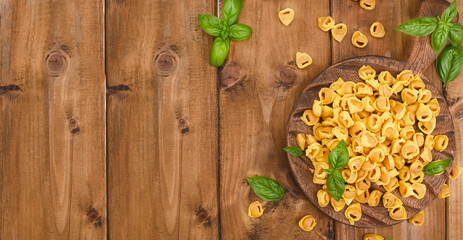 Tortellini on a wooden board with basil and parmesan. Specialties of the cuisine from Bologna and Emilia Romagna: Cappelletti, fresh egg pasta with meat and vegetables filling. banner. 