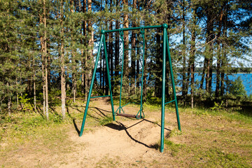 Fototapeta premium A freestanding green swing in a wooded area. A lake in the background. Children's entertainment.
