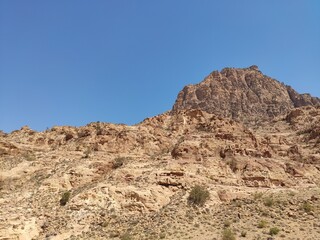 Fototapeta na wymiar Dana, la plus grande réserve naturelle de Jordanie, marche en plein milieu d'une zone montagneuse rouge et blanche, avec un peu de verdure et de la forte chaleur, sans ombre, montagnes escalader