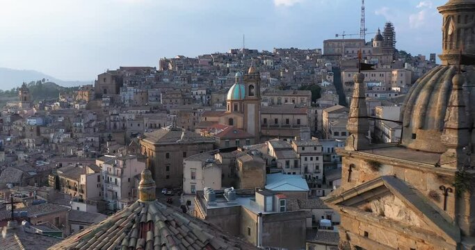 Flying over an ancient bell tower and its spiers in Caltagirone with a view of the historical center, a dome and the famous ceramic decorated stairs in Sicily, south of Italy
