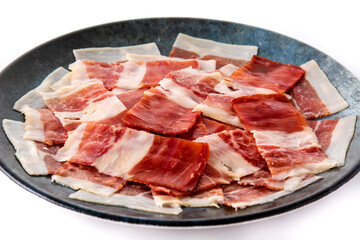 Spanish serrano ham slice on black plate isolated on white background
