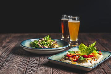 Two glass of beer and autumn or fall food over black background on rustic wooden table.