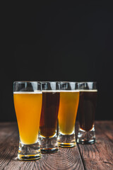 Different kinds of cold beer on a rustic wooden table over black background.