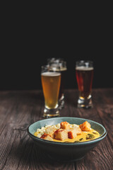 Two glass of beer and autumn or fall food over black background on rustic wooden table.