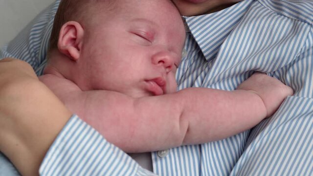 motherhood, childhood, family, care, health, maternity concept - nake newborn wrapped in warm blue blanket sleeping on mother chest arm hands. Mum relax holding kiss hug carring infant baby at home