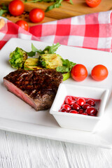 Restaurant food closeup on served table. Perfect juicy beef steak with vegetables and cranberry sauce.