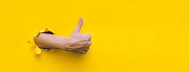 The right female hand shows a thumb up gesture (like). Torn hole in yellow paper. The concept of...