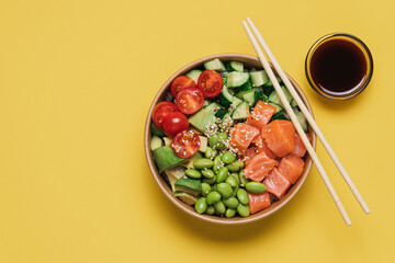 Salmon, avocado, cucumber, tomato, edamame beans and rice poke bowl on yellow background