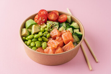 Salmon, avocado, cucumber, tomato, edamame beans and rice poke bowl on pink background
