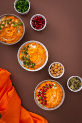 Pumpkin puree soup of butternut squash in bowls with chickpeas and green onions, pumpkin and pomegranate seeds, top view on plates with food on brown background