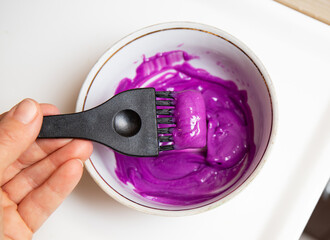 Ceramic bowl with mixed pastel purple hair dye, inside is dye brush, hair coloring brush. 