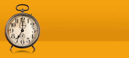 Closeup of an old alarm clock on orange and yellow background with copy space and reflections, seven o'clock. Italy.