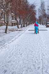 Fototapeta na wymiar A woman with a child in a sleigh walks on a snow-covered sidewalk