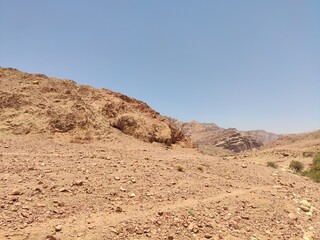 Fototapeta na wymiar Dana, la plus grande réserve naturelle de Jordanie, marche en plein milieu d'une zone montagneuse rouge et blanche, avec un peu de verdure et de la forte chaleur, sans ombre, parcourir desert cailloux