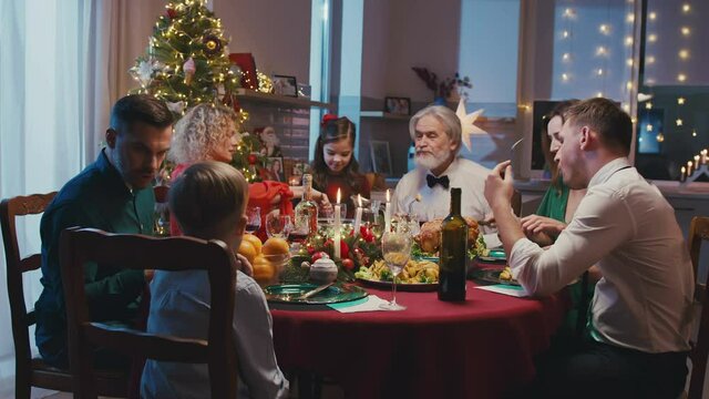 Happy caucasian family celebrating Christmas, chatting at dinner party table. Beautiful friends having Christmas dinner party at home, eating delicious food.