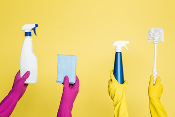 cropped view of cleaners holding spray bottles with detergent, rag and toilet brush isolated on yellow