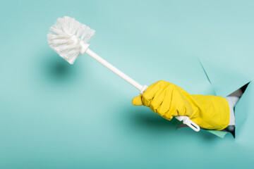partial view of cleaner in rubber glove holding toilet brush through hole in paper wall on blue