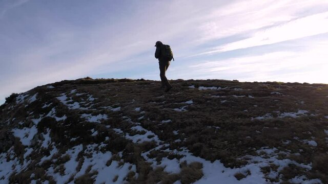 Young man walking on top of the mountain in autumn season with early snow. Standing on the ridge. Alone in the mountains. Hike and travel with backpack. Sunset light on the summit.