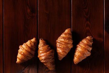 Several croissants lie on a brown wooden table. Empty space for text. View from above.