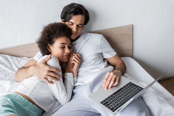 high angle view of african american woman sleeping on chest of boyfriend with laptop